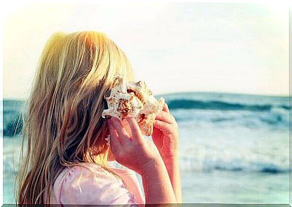 child listening to a shell in front of the sea